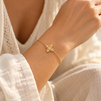 Bracelet Aylin porté au poignet, chaîne fine dorée et motif ajouré à quatre pierres blanches, vêtement écru et lumière naturelle.
